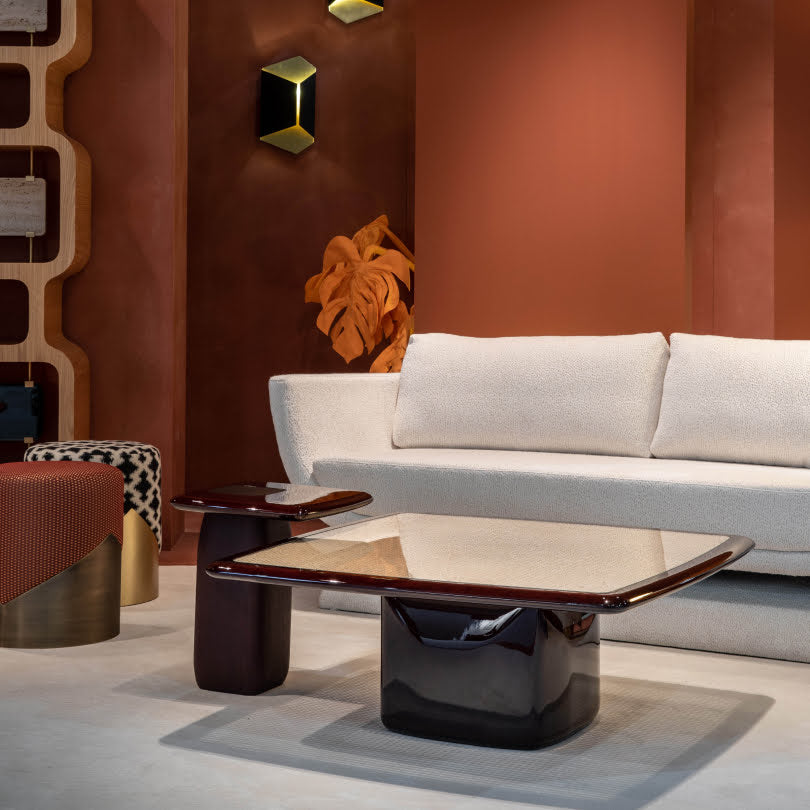 A warm-toned living space featuring a sleek, glossy coffee table and side table with sculptural bases, paired with a neutral curved sofa.