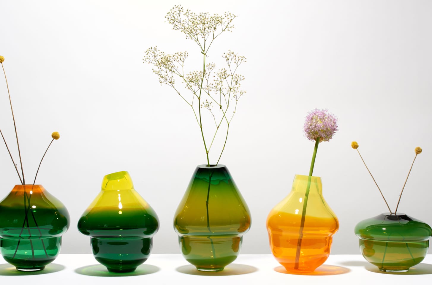 A row of green and amber glass vases with delicate flowers.