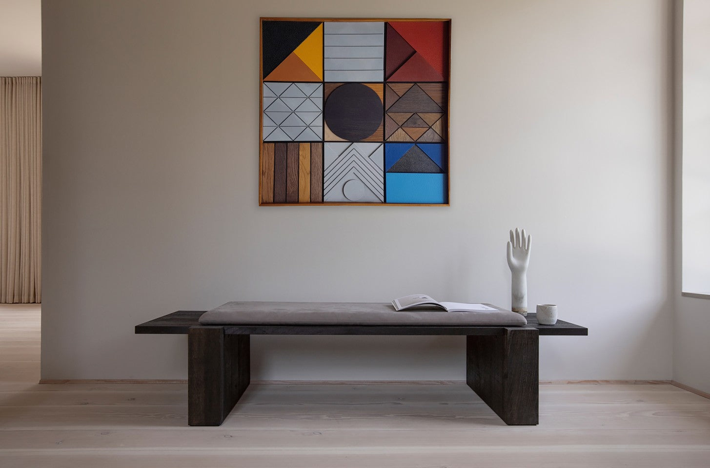 A minimalist interior featuring a dark wood bench with a cushioned seat, a geometric wall artwork, and carefully placed decor, creating a balanced, modern aesthetic.
