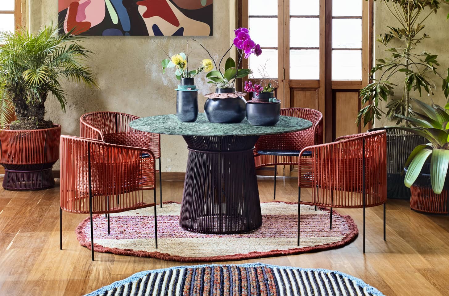 A vibrant dining space with woven chairs, a round table, and lush greenery.