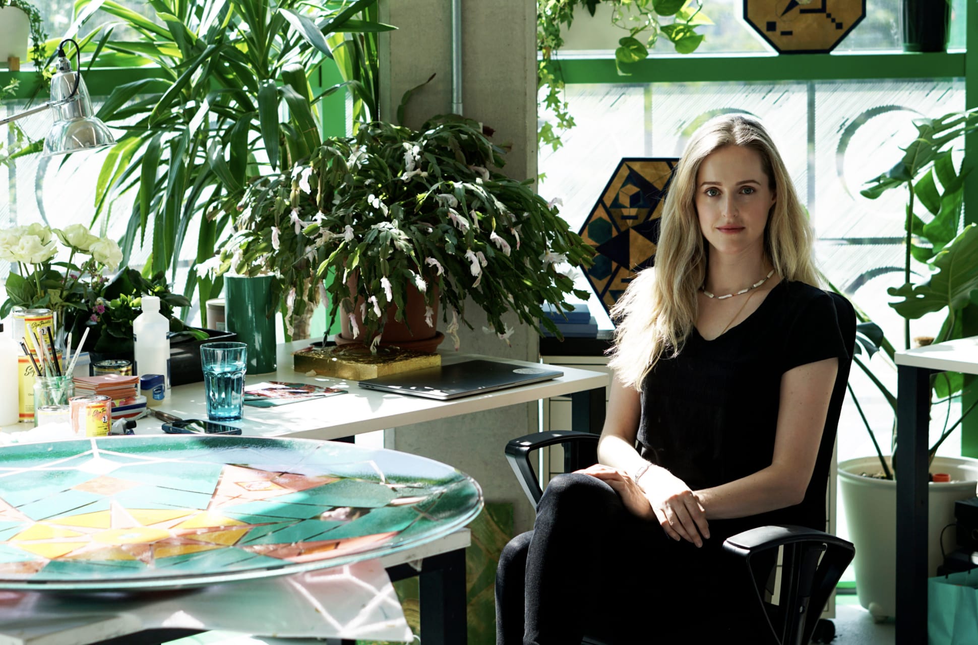 Anastasya Martynova seated in her studio, surrounded by plants and artwork.