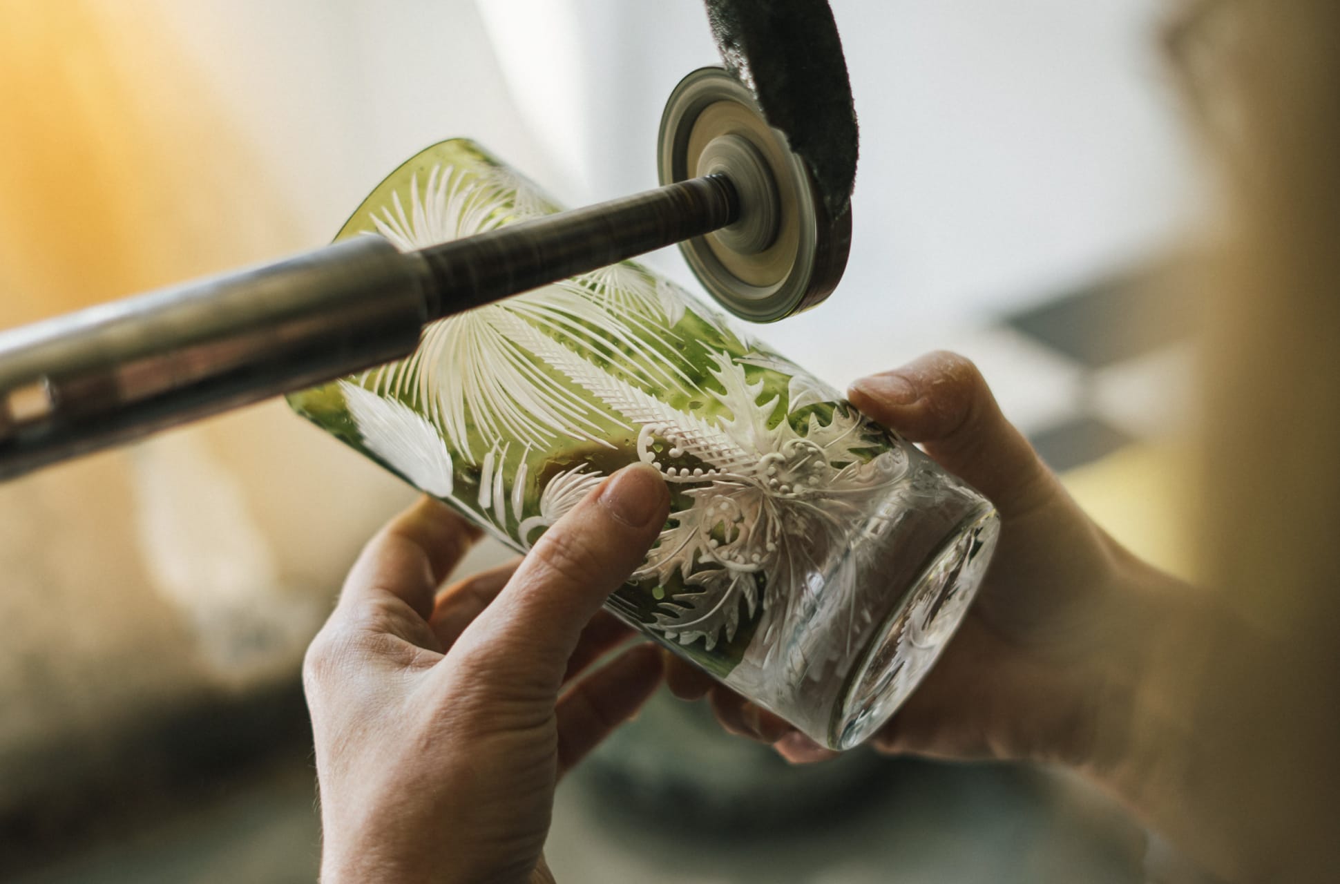 Close-up of a craftsman using a rotary tool to etch a delicate design onto glass.