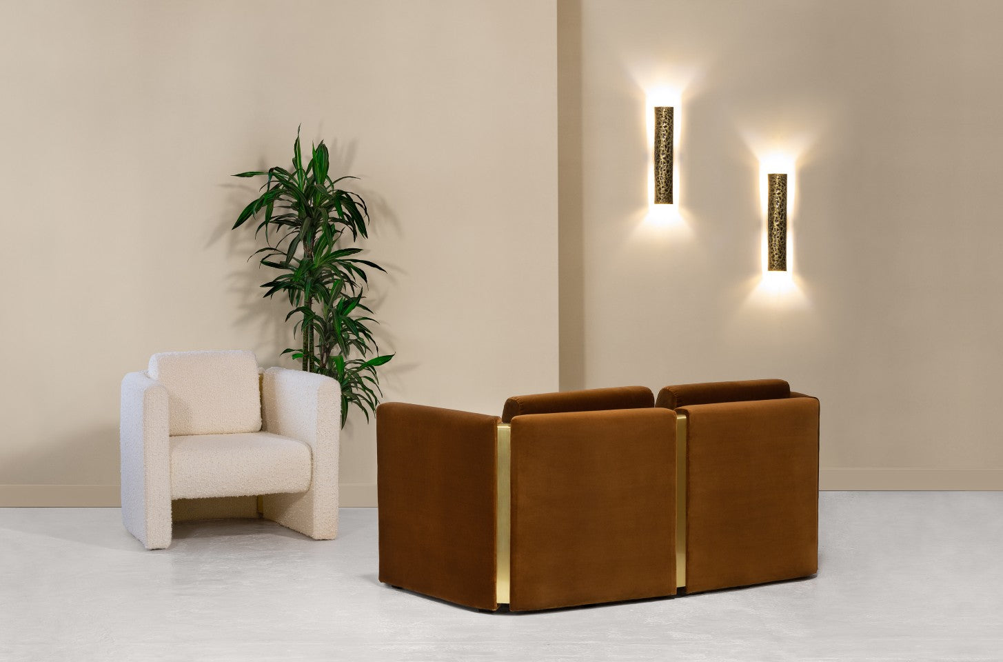 A modern seating area featuring a white bouclé armchair, a modular velvet sofa with gold accents, ambient wall sconces, and a green plant.