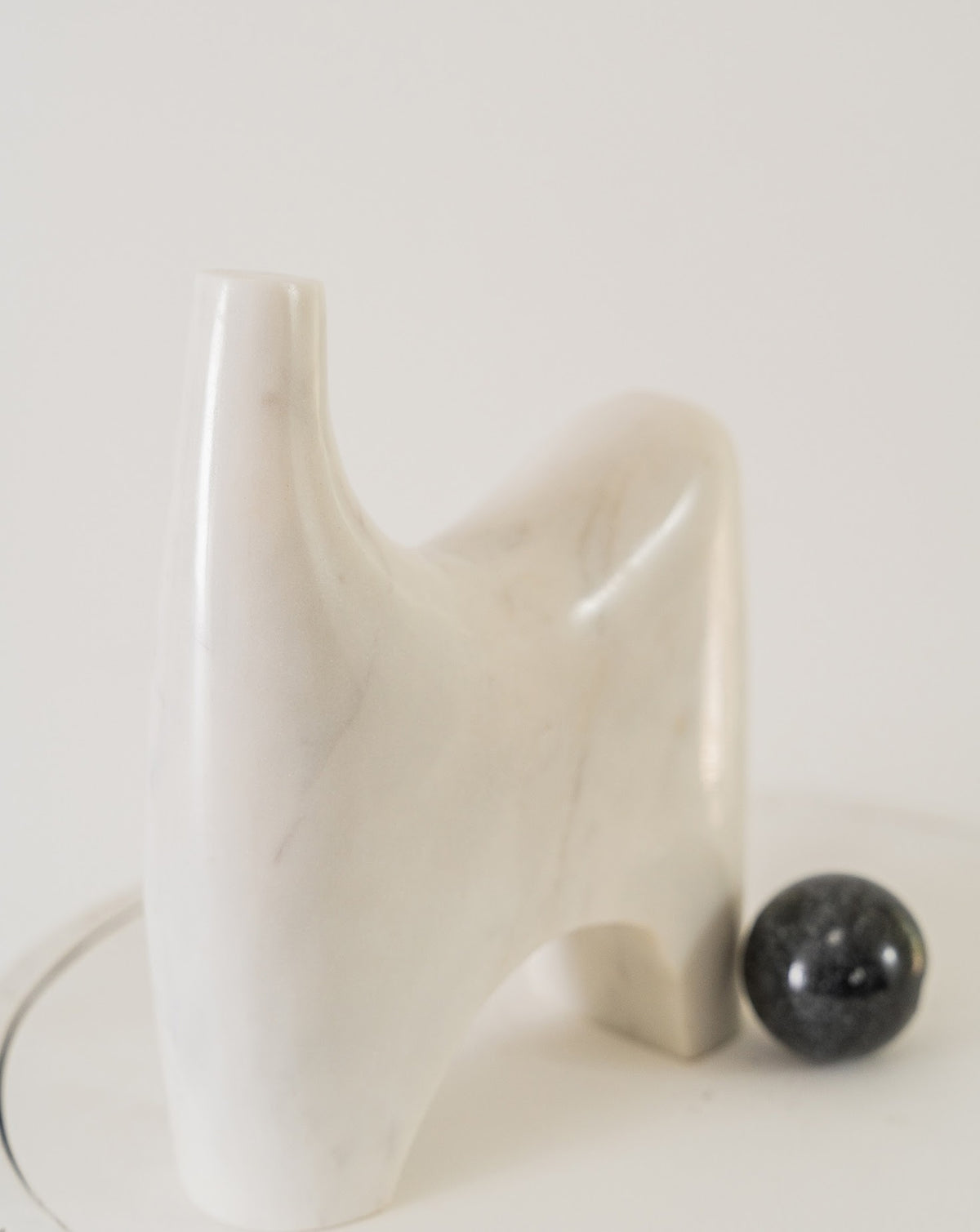 Polished black marble sphere resting beneath the white marble arch, a study in contrast
