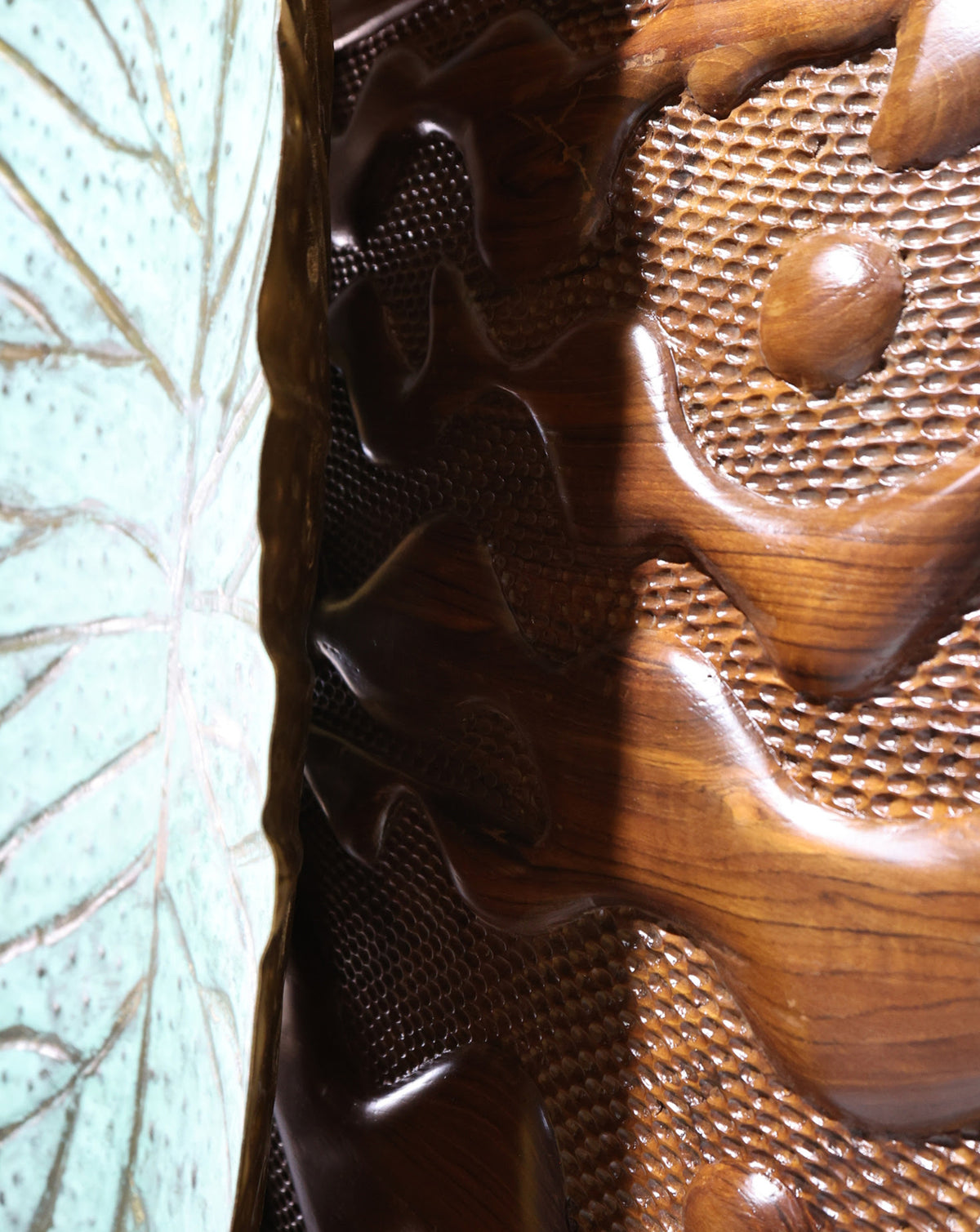 Hand carved teak panel in brown and green, shaped like a leaf over rolling terrain