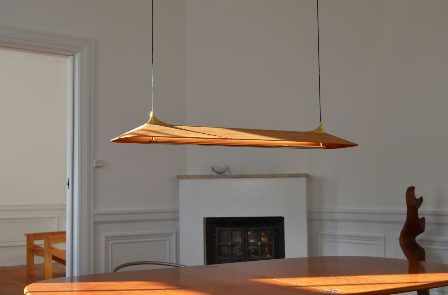 A sleek wooden and brass pendant light elegantly suspended over a dining table, casting warm tones in a minimalist interior with classic detailing.