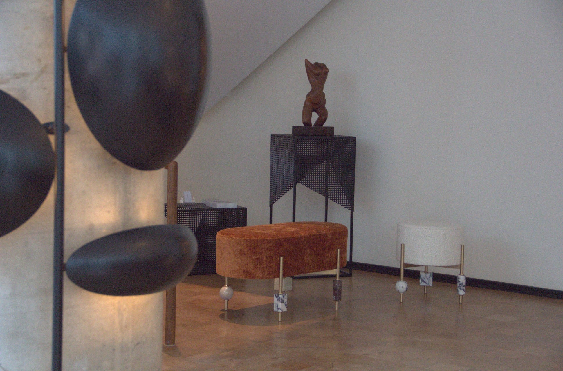 A contemporary interior with modern sculptural furniture pieces, featuring a rust-colored velvet bench and a white boucle stool with brass and marble legs, set against a neutral wall with geometric decor.