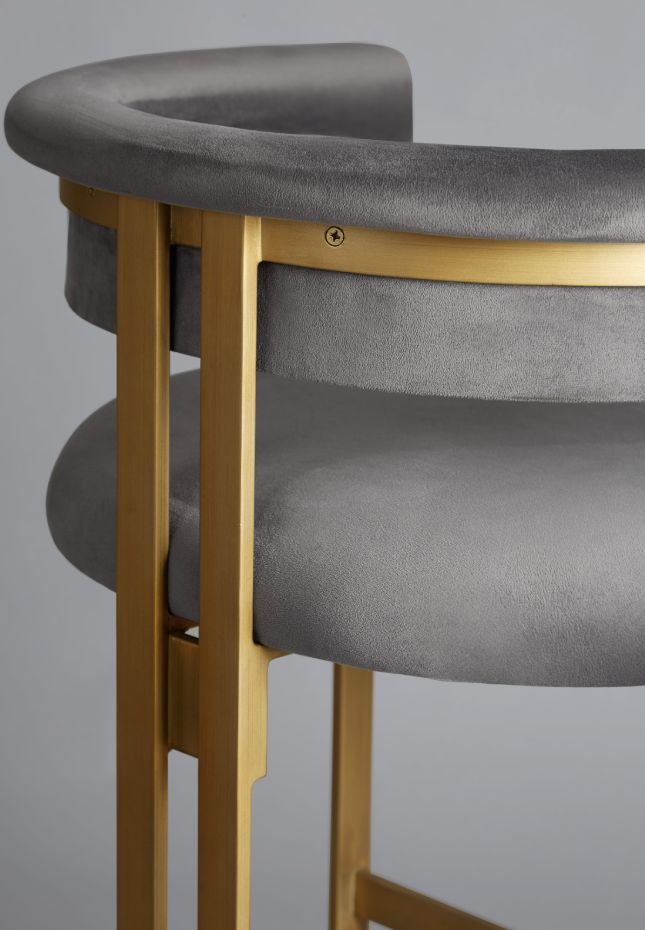 A close-up of a luxurious barstool featuring plush grey velvet upholstery and a sleek gold metal frame, showcasing elegant curves and refined craftsmanship.