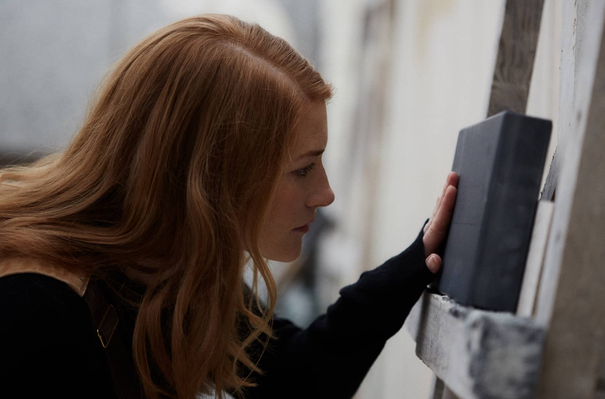 Zoe Wilson closely inspecting a black stone slab, her hand resting on it as she examines its surface with focused attention.