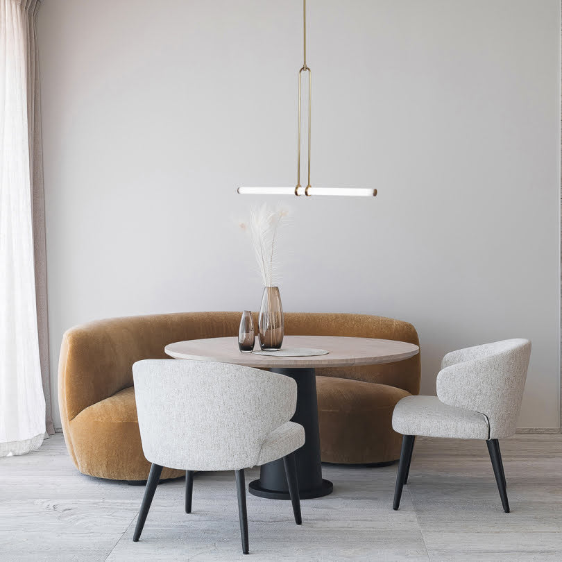 Modern dining area with a round table, brown curved sofa, gray chairs, and a pendant light.