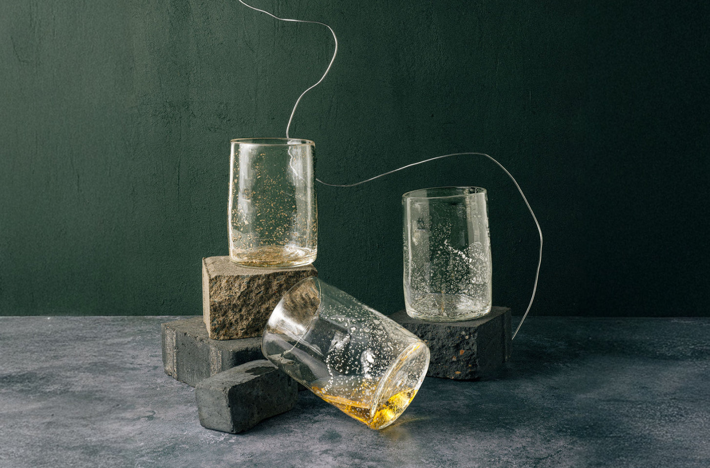 Clear glass tumblers with bubble texture on a dark surface and green background
