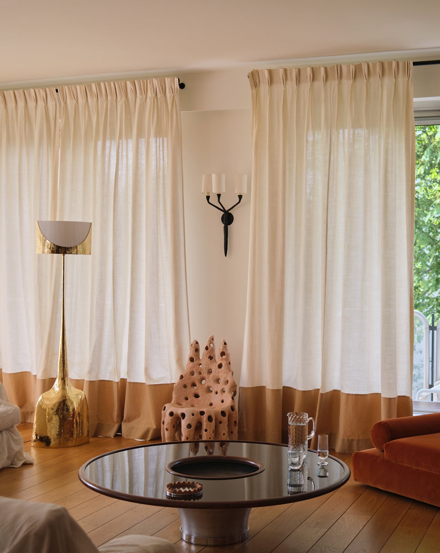 Living room with large windows, beige curtains, a round glass table, and a chair.