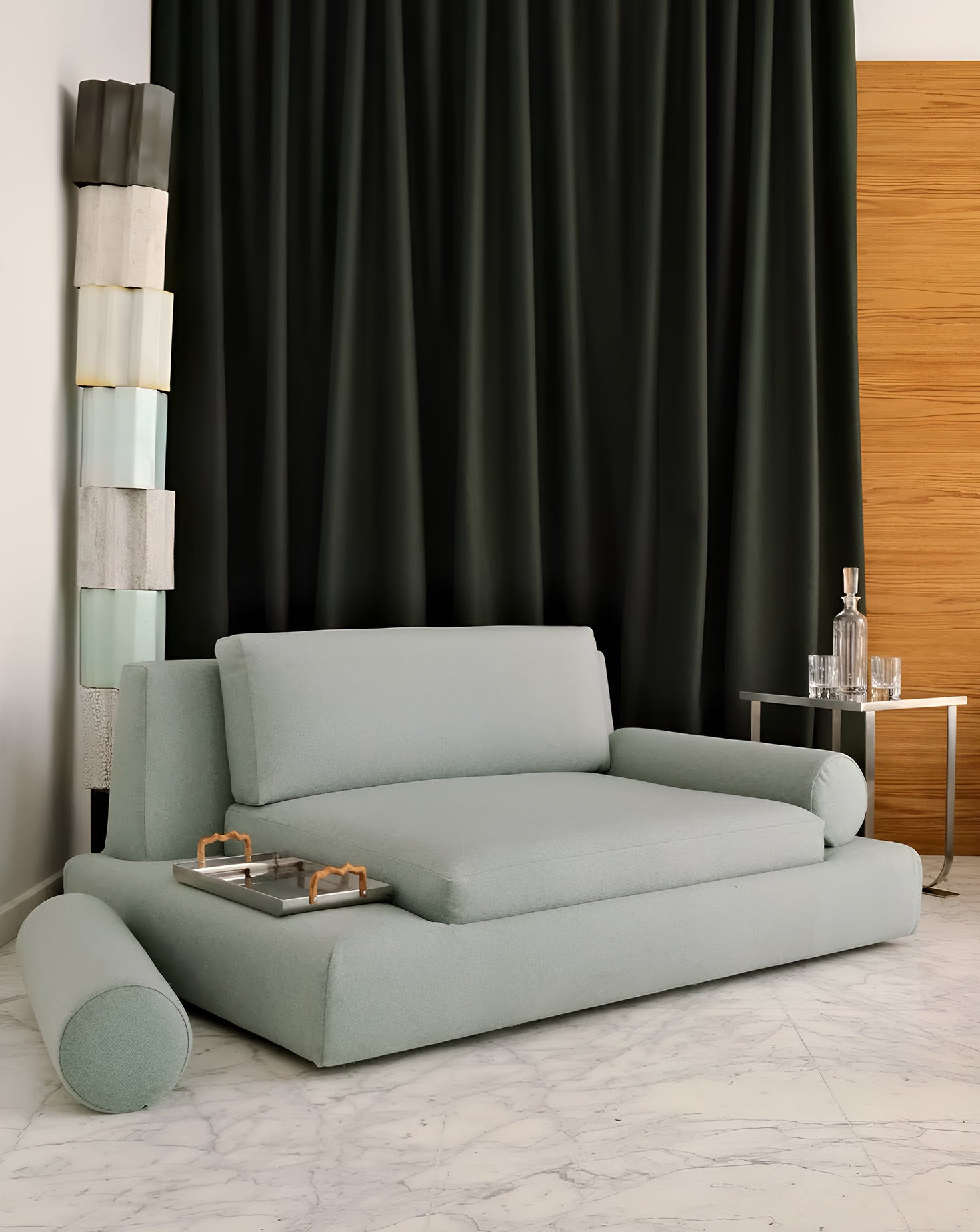 Light blue sofa in a room with black curtains and a wooden side table.